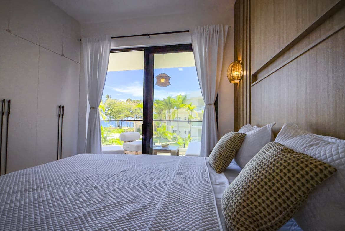 Luxury bedroom with king-size bed, ocean view balcony, and modern decor.