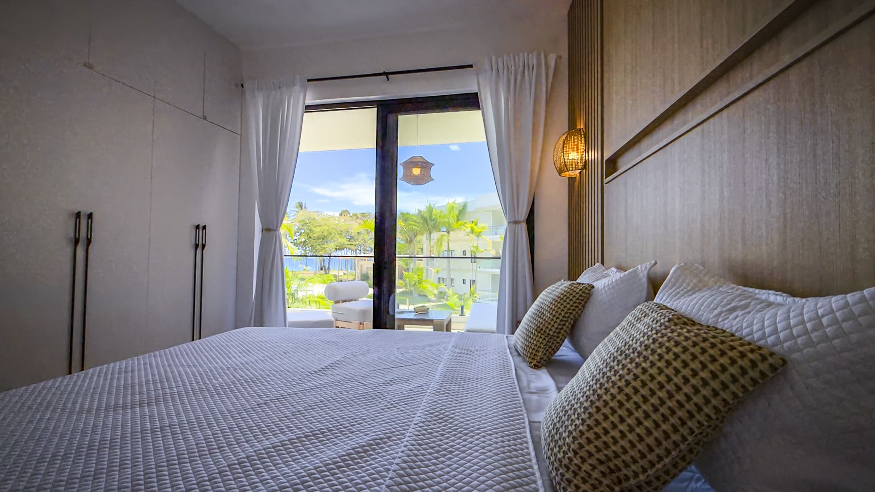 Luxury bedroom with king-size bed, ocean view balcony, and modern decor.