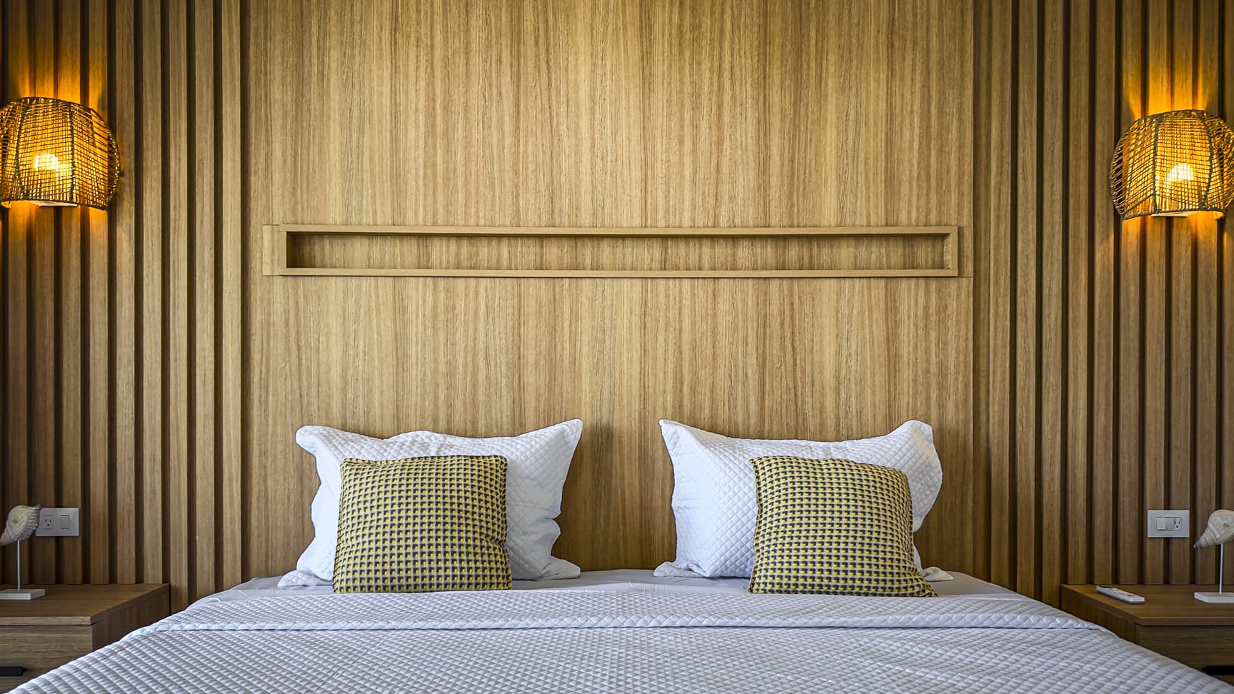 Cozy bedroom with a wooden headboard, textured pillows, and woven lamps.