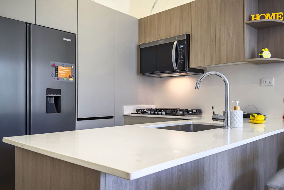 Modern kitchen with stainless steel refrigerator, white countertop, and wooden cabinets.