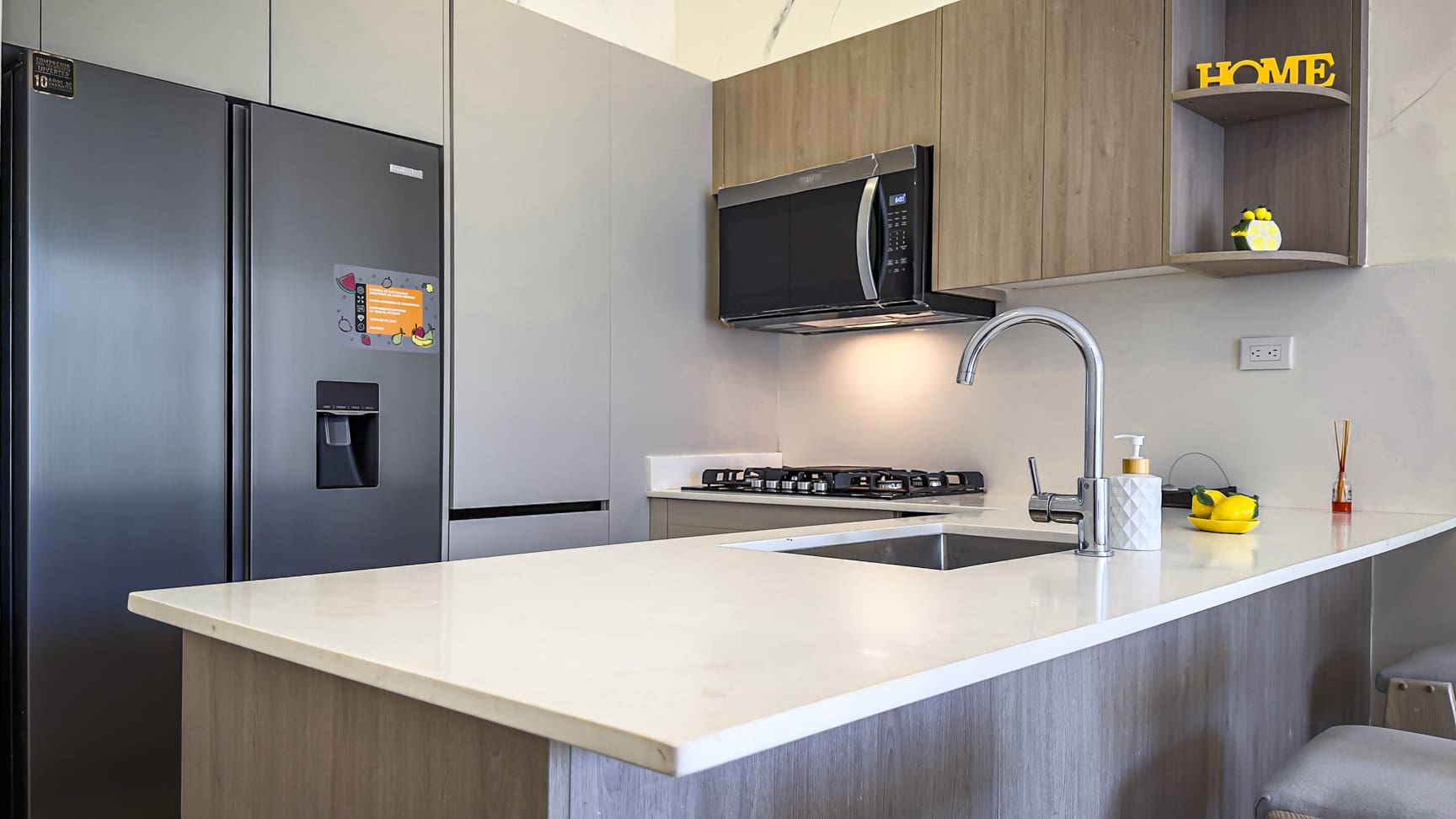 Modern kitchen with stainless steel refrigerator, white countertop, and wooden cabinets.