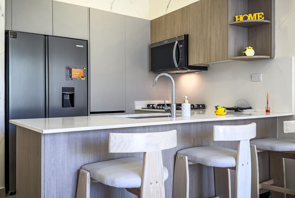 Modern kitchen island with bar stools, stainless steel refrigerator, and microwave.