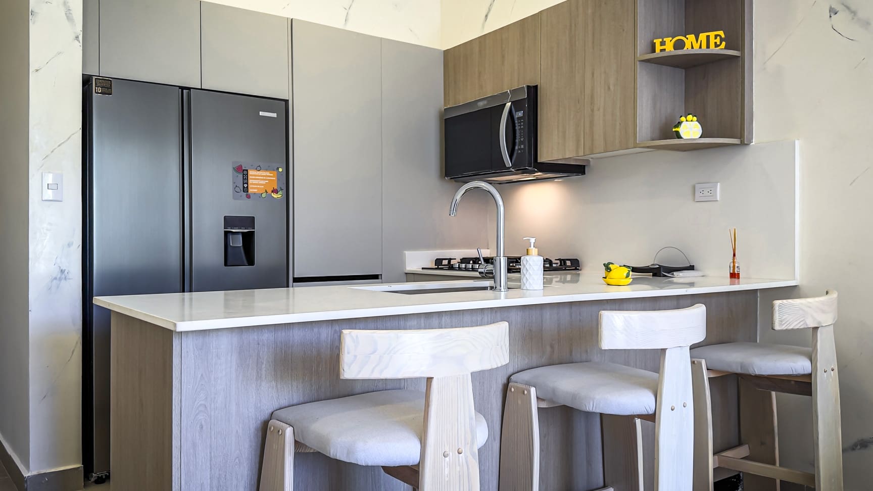 Modern kitchen island with bar stools, stainless steel refrigerator, and microwave.