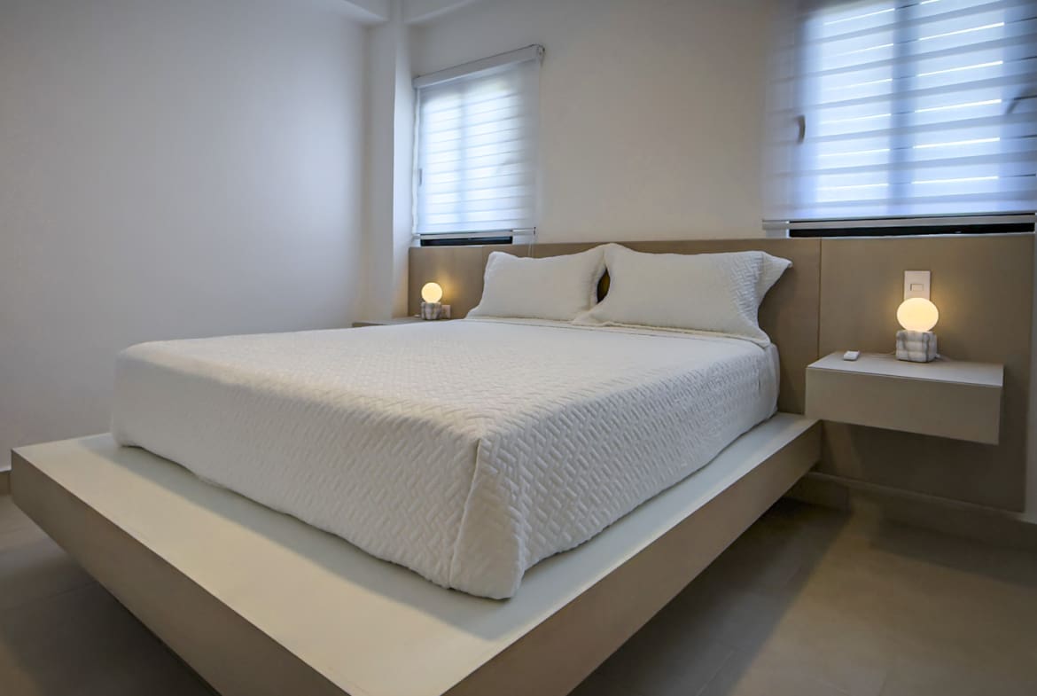 Modern bedroom with minimalist white bed, neutral tones, and ambient bedside lamps.