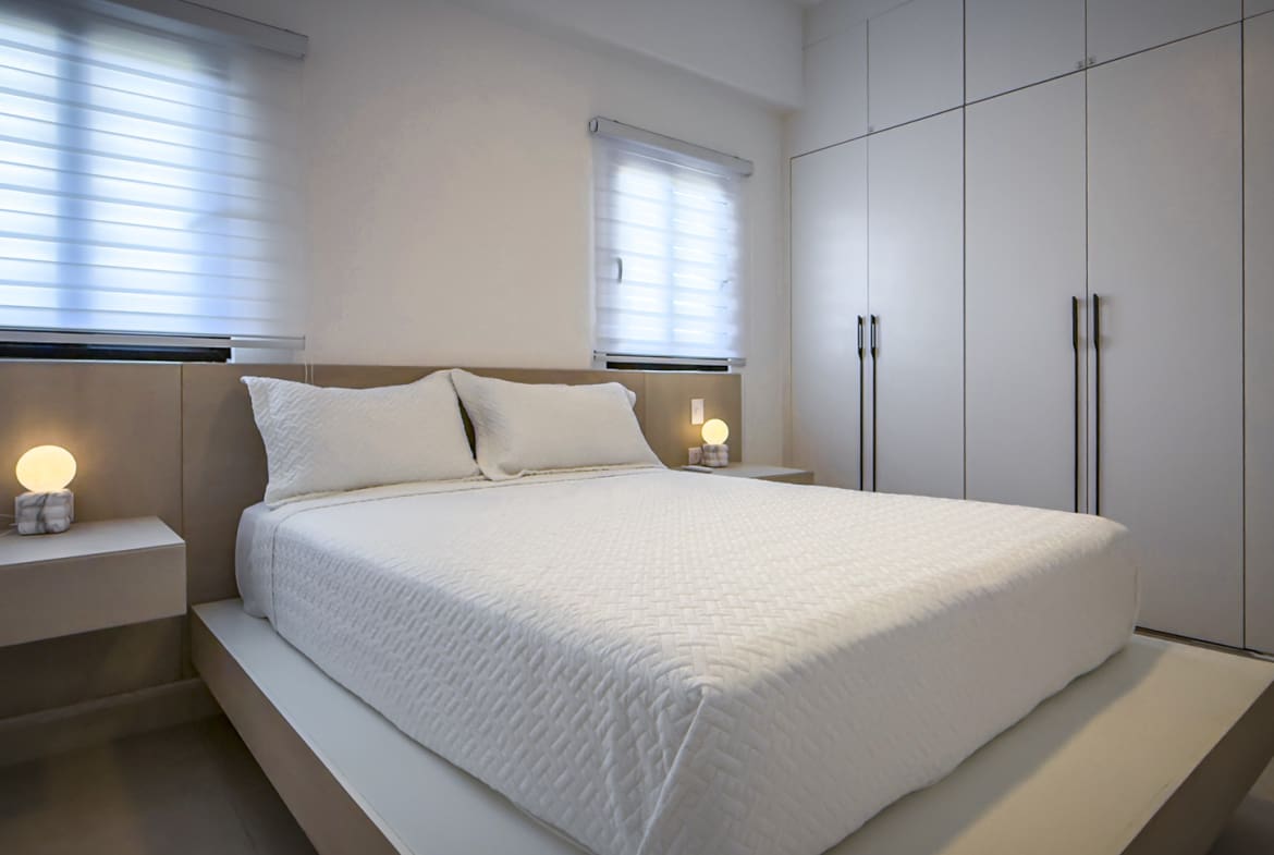 Modern white bedroom with a large bed, minimalist nightstands, and built-in wardrobe.