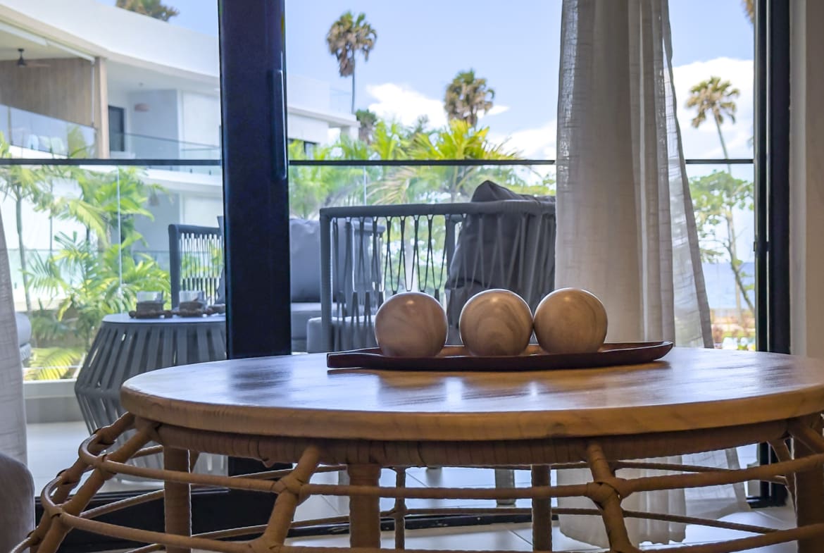 Wooden table with decorative spheres in a room with a balcony view of palm trees.