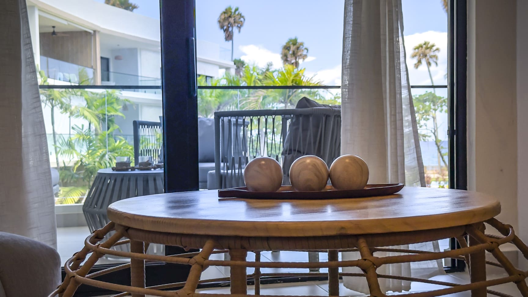 Wooden table with decorative spheres in a room with a balcony view of palm trees.