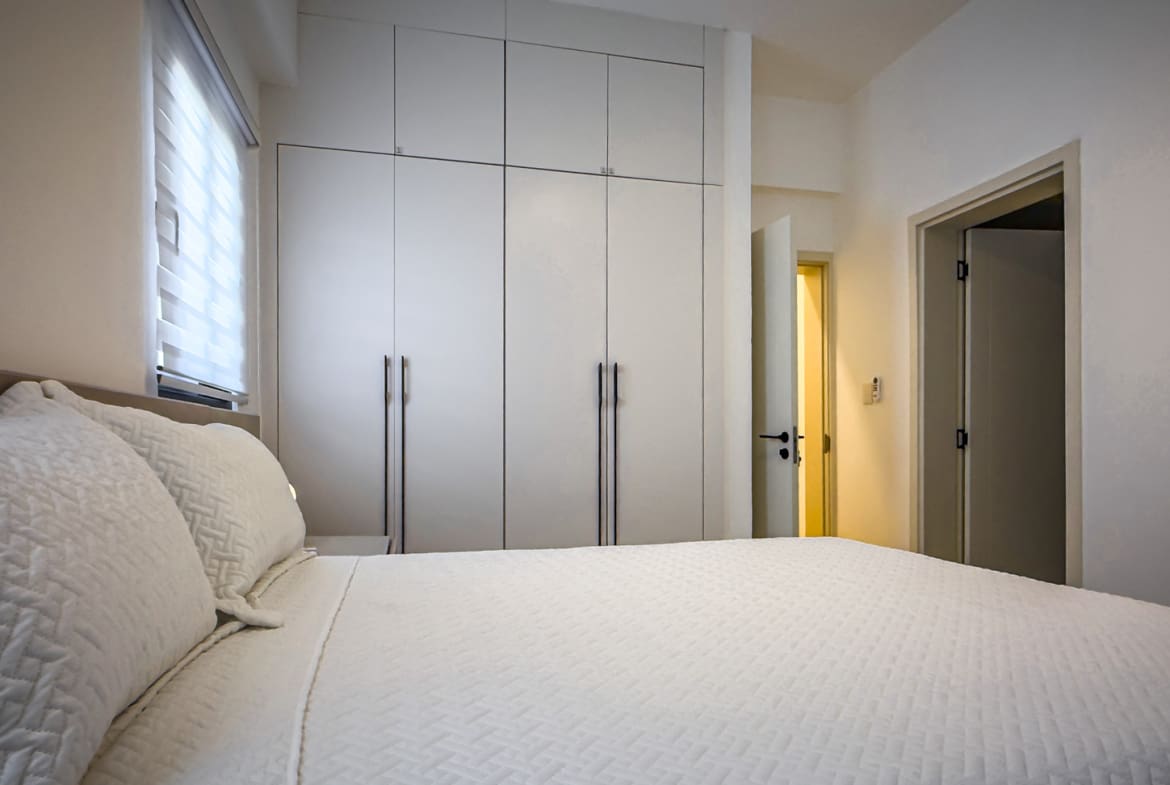 Modern bedroom with white built-in wardrobes and a bed with white linens.