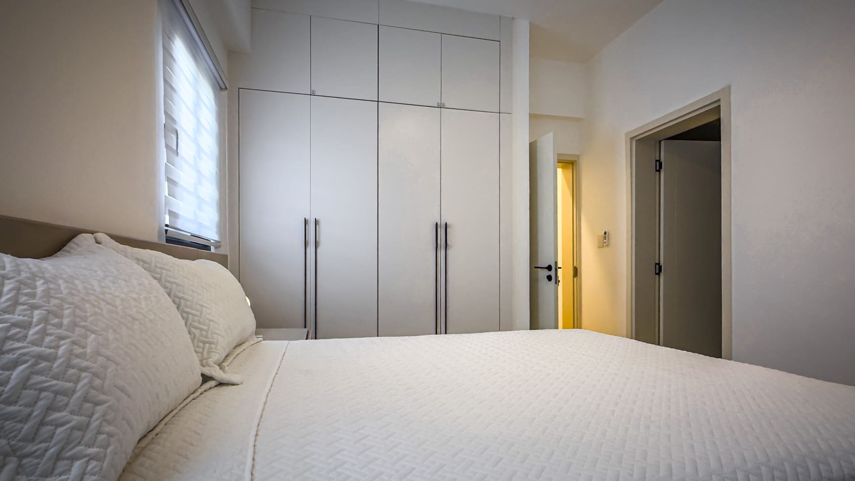 Modern bedroom with white built-in wardrobes and a bed with white linens.
