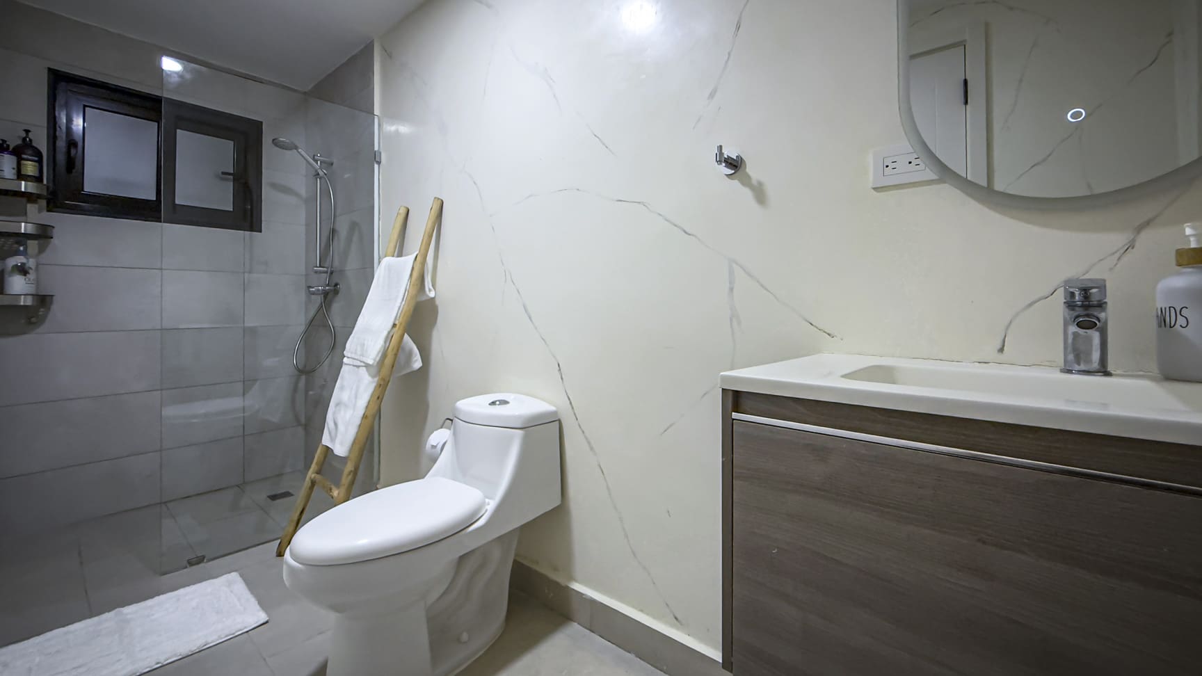 Modern bathroom with white marble walls, a walk-in shower, and a wooden ladder towel rack.