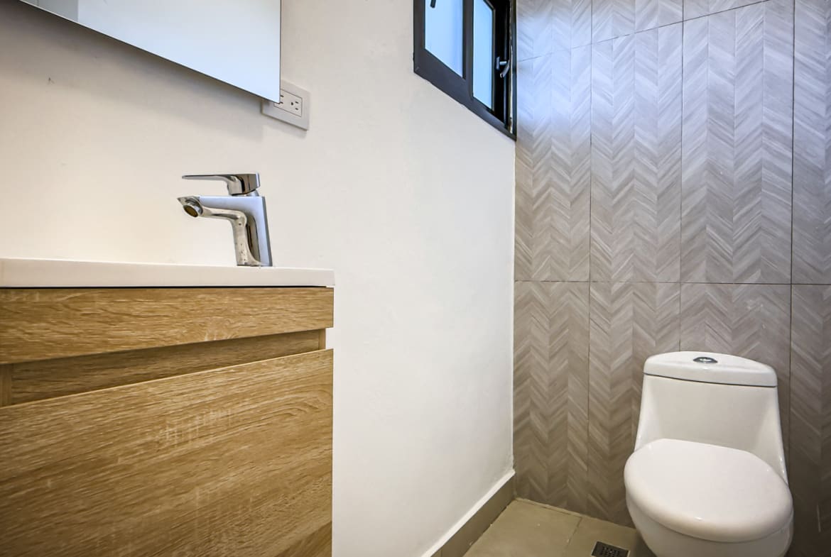 Modern bathroom with wood vanity, chrome faucet, and geometric tile wall.