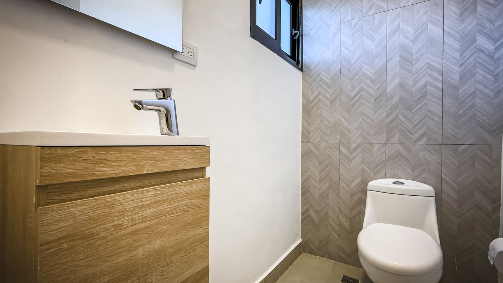 Modern bathroom with wood vanity, chrome faucet, and geometric tile wall.