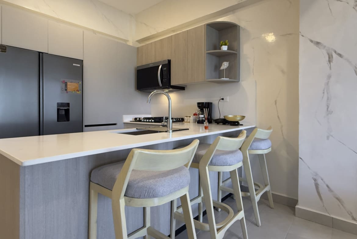 Modern kitchen with light wood cabinets, stainless steel appliances, and a breakfast bar with stools.