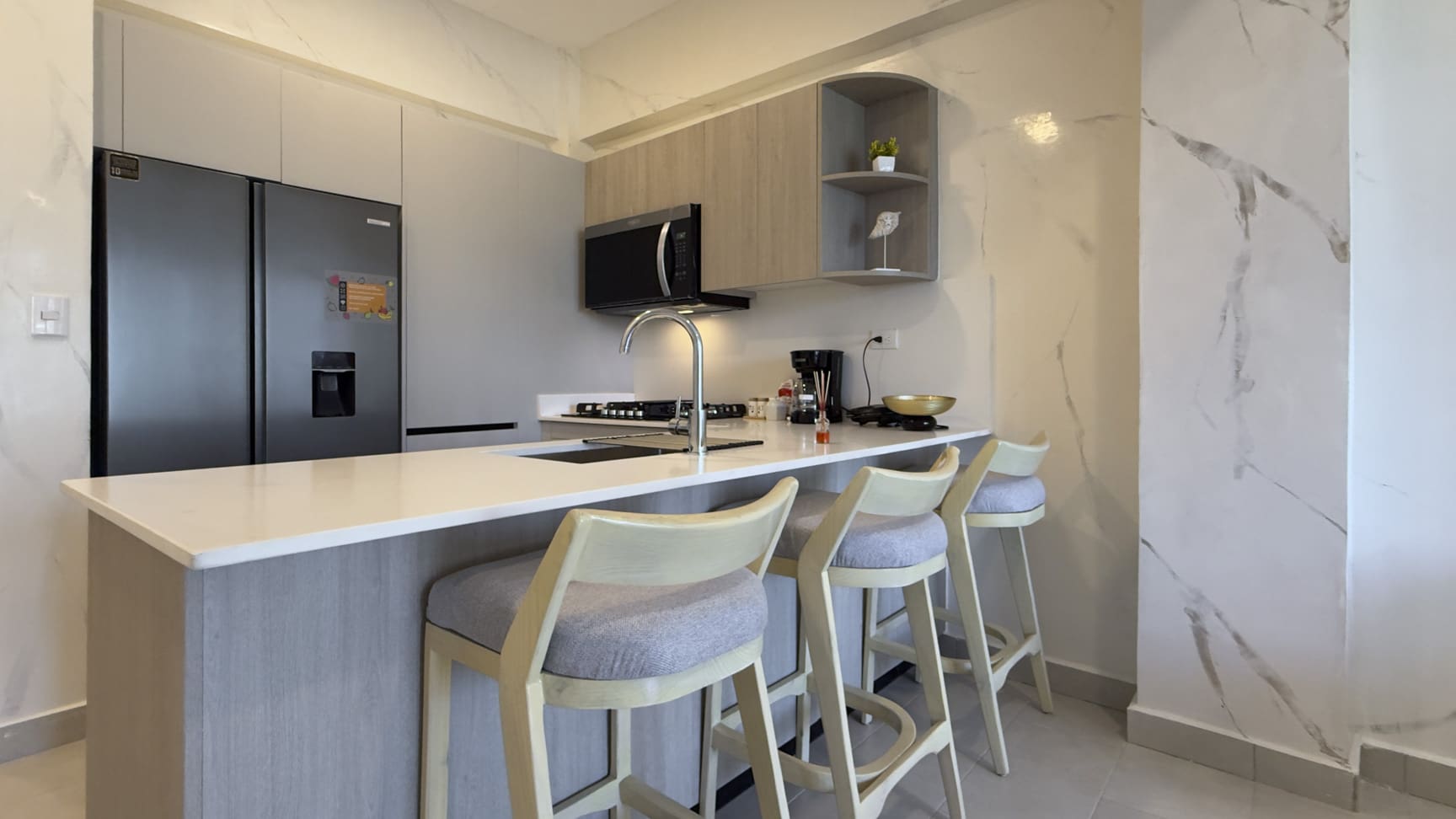 Modern kitchen with light wood cabinets, stainless steel appliances, and a breakfast bar with stools.