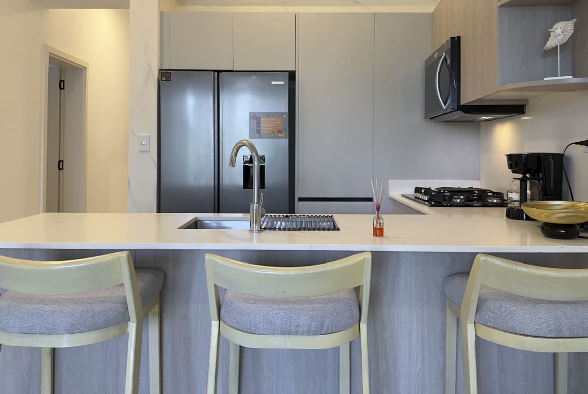 Modern kitchen island with bar stools, stainless steel refrigerator, and coffee maker.