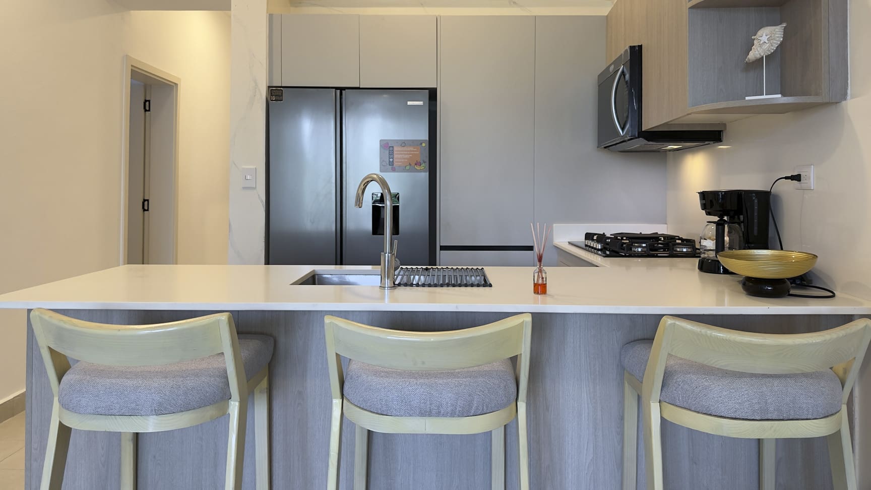 Modern kitchen island with bar stools, stainless steel refrigerator, and coffee maker.