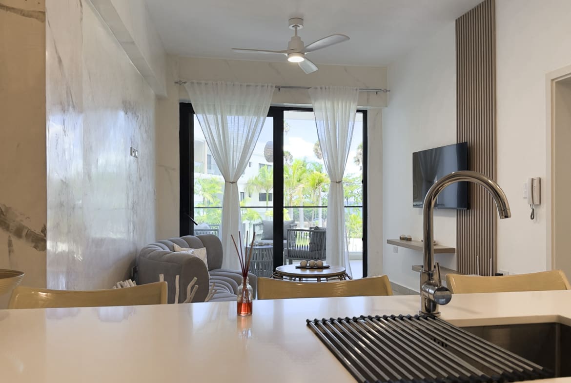 Modern kitchen island with sink overlooks a bright living room with balcony views