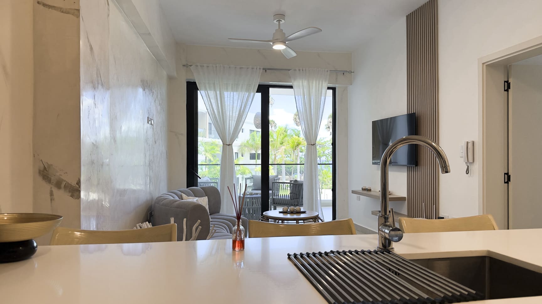 Modern kitchen island with sink overlooks a bright living room with balcony views