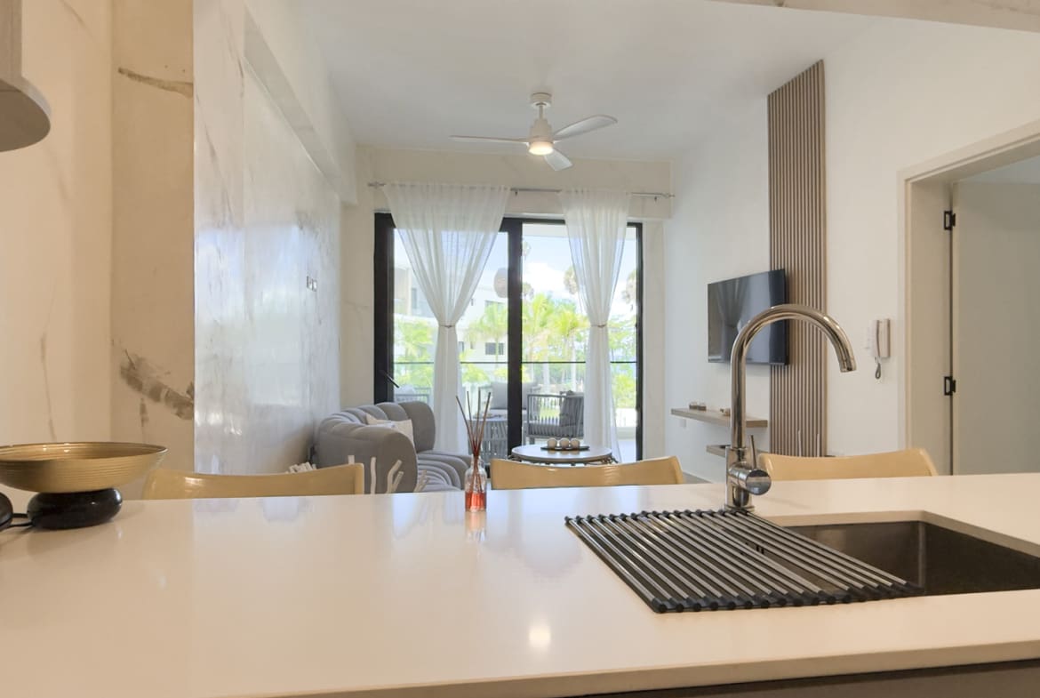 Modern kitchen counter with sink and faucet, overlooking a living area with sofa and balcony.