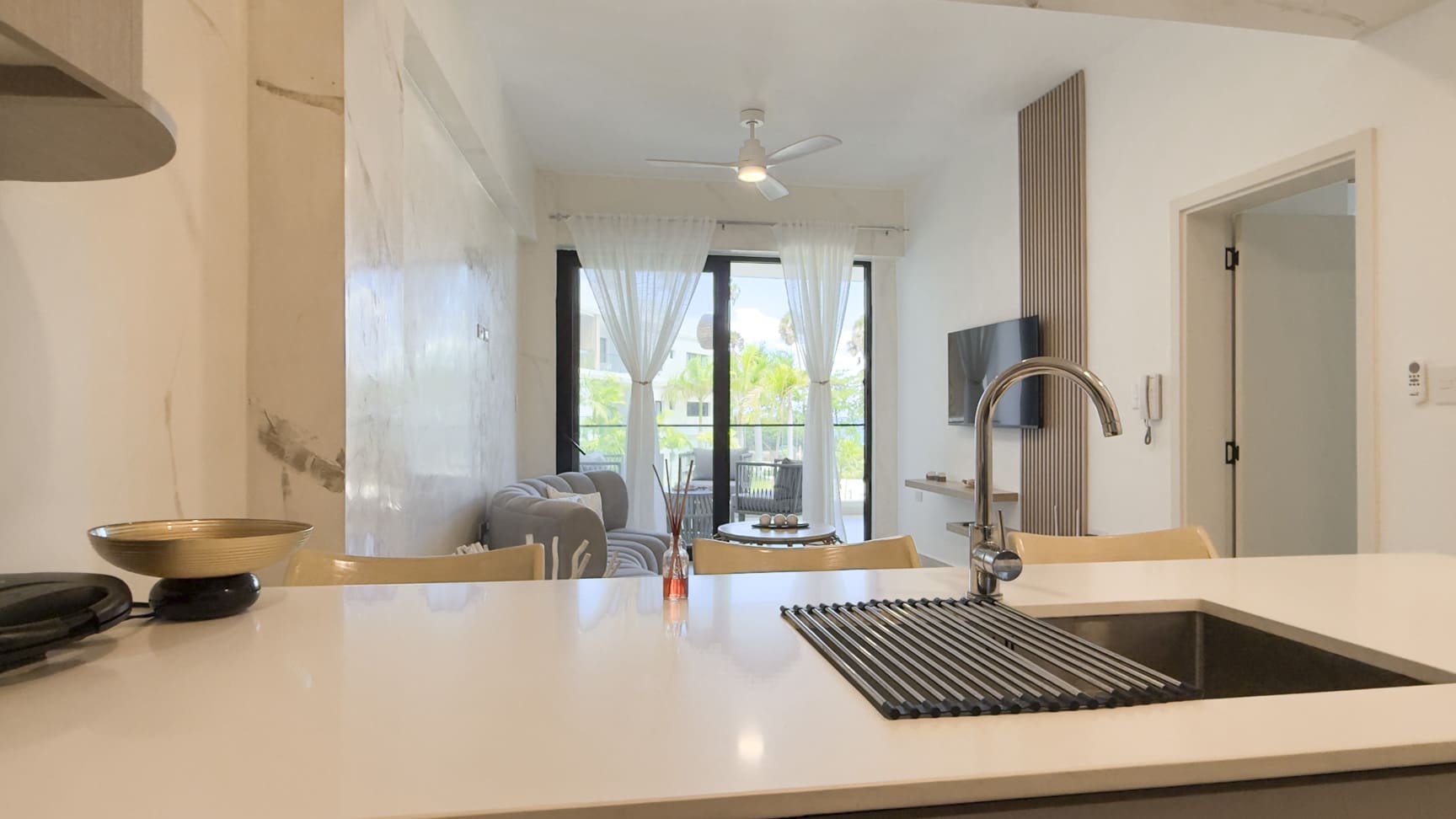 Modern kitchen counter with sink and faucet, overlooking a living area with sofa and balcony.