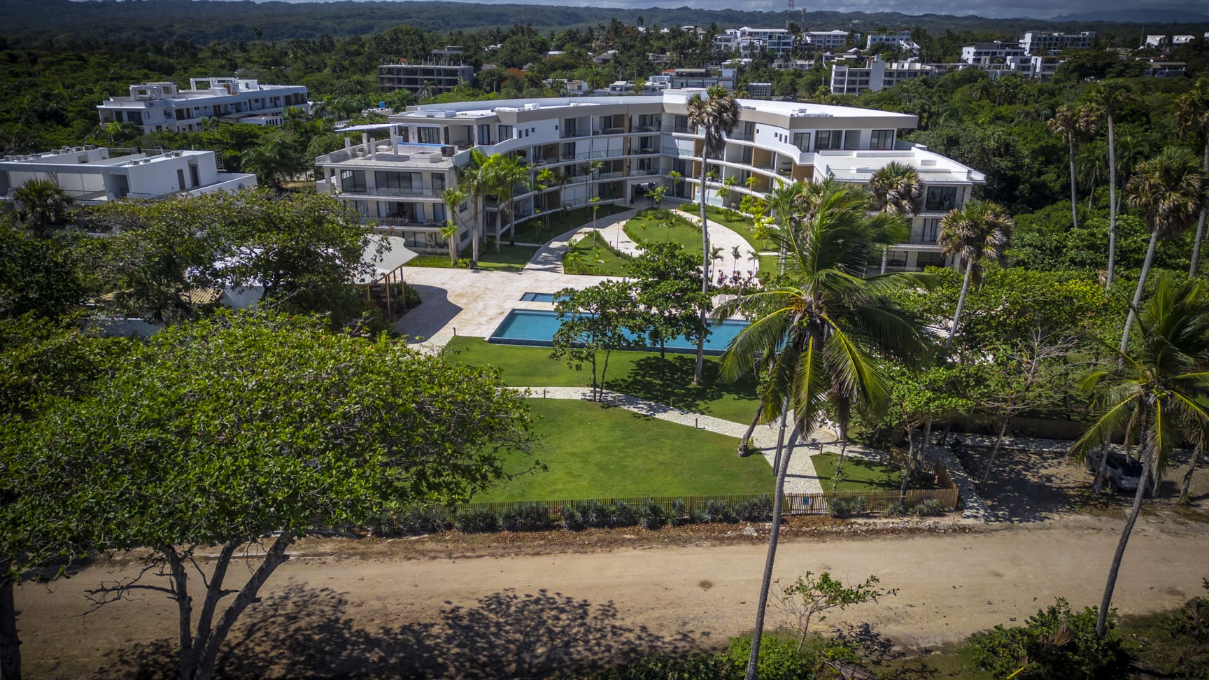 Aerial view of a modern resort with a swimming pool and palm trees.