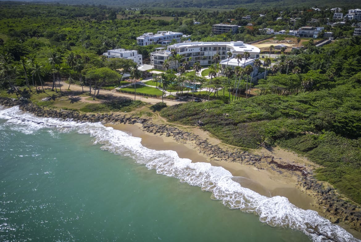 Aerial view of a modern resort complex on a tropical coastline with turquoise ocean waves.