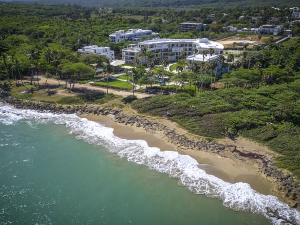 Aerial view of a modern resort complex on a tropical coastline with turquoise ocean waves.
