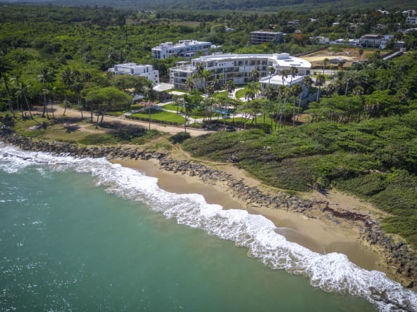 Aerial view of a modern resort complex on a tropical coastline with turquoise ocean waves.