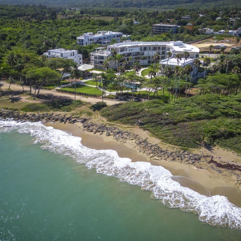 Aerial view of a modern resort complex on a tropical coastline with turquoise ocean waves.