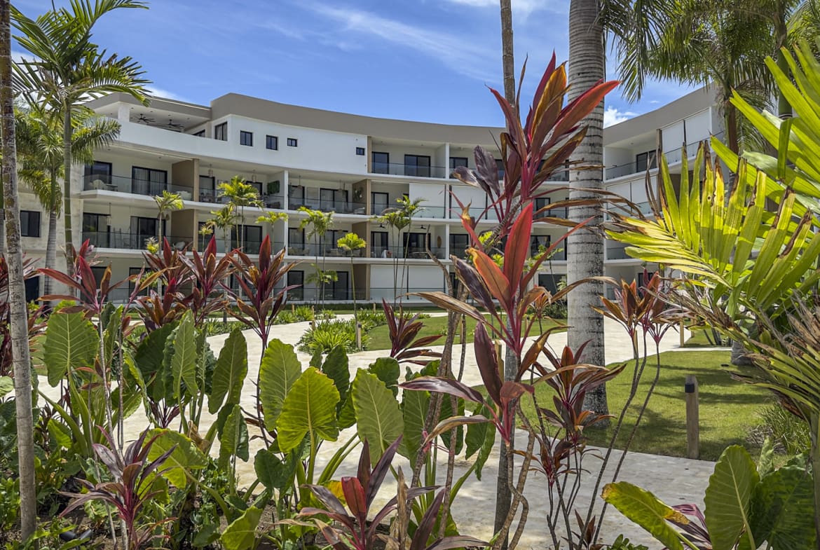 Modern resort building with lush tropical landscaping and palm trees.