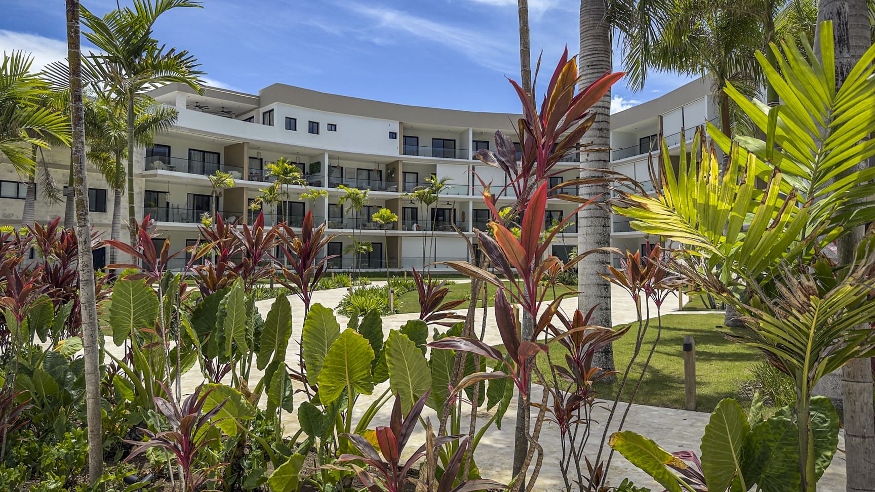 Modern resort building with lush tropical landscaping and palm trees.