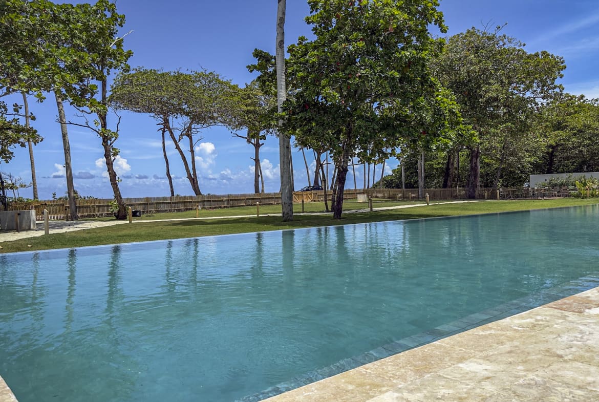 Infinity pool overlooking a tropical beach with palm trees and lush greenery.