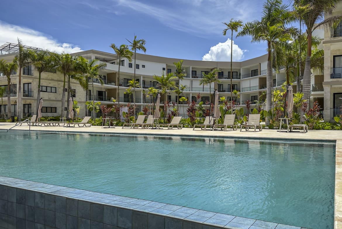 Resort pool with lounge chairs and palm trees outside modern hotel.