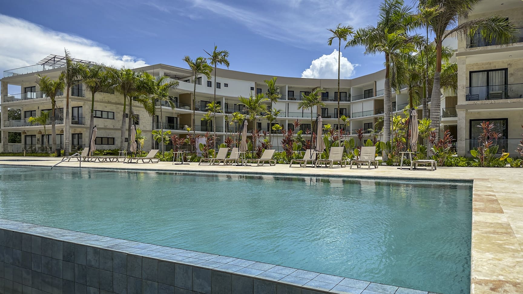 Resort pool with lounge chairs and palm trees outside modern hotel.
