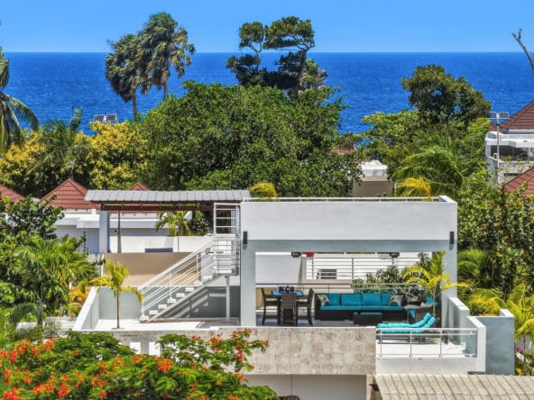 Modern rooftop terrace with ocean view, turquoise seating, and lush tropical foliage.