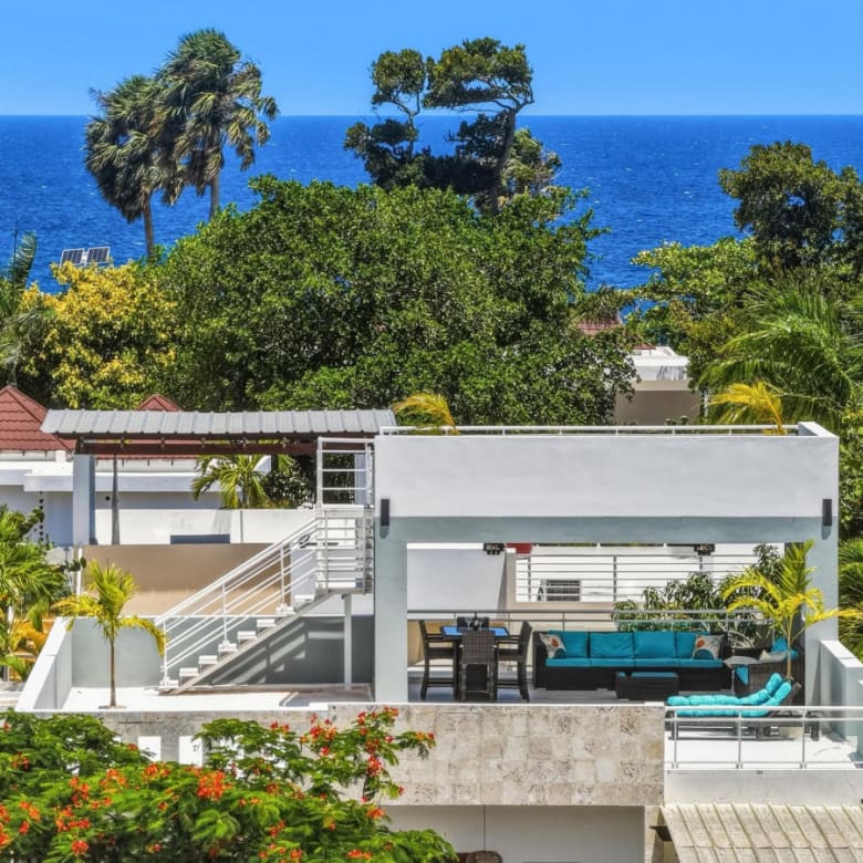 Modern rooftop terrace with ocean view, turquoise seating, and lush tropical foliage.