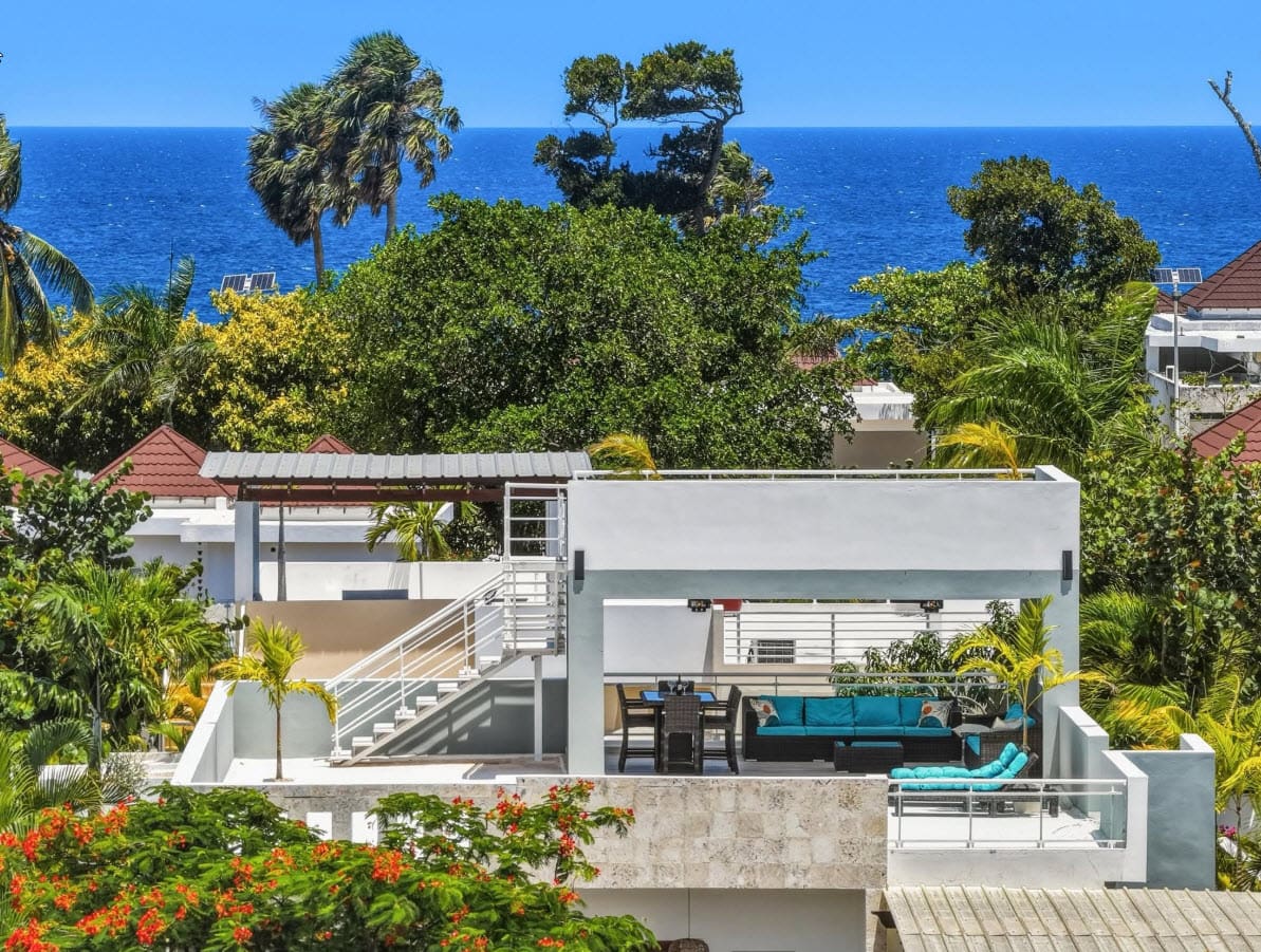 Modern rooftop terrace with ocean view, turquoise seating, and lush tropical foliage.