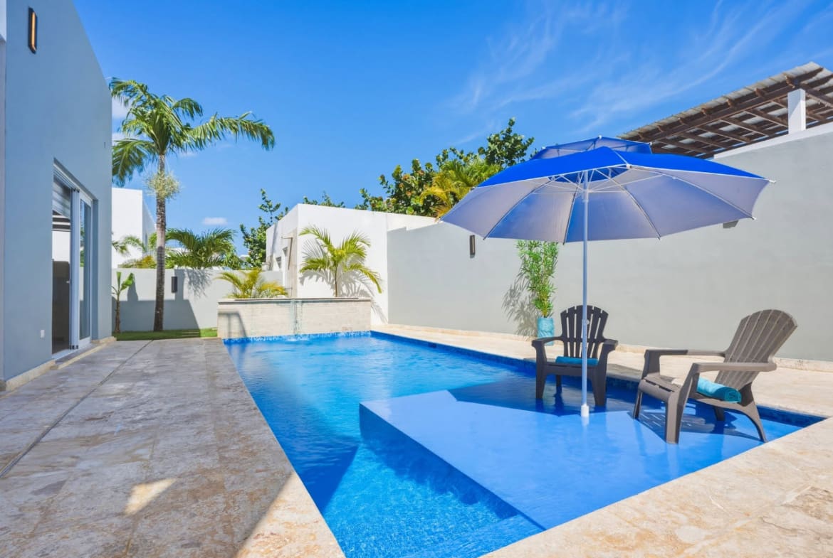 Modern villa with a bright blue swimming pool, lounge chairs, and umbrella.