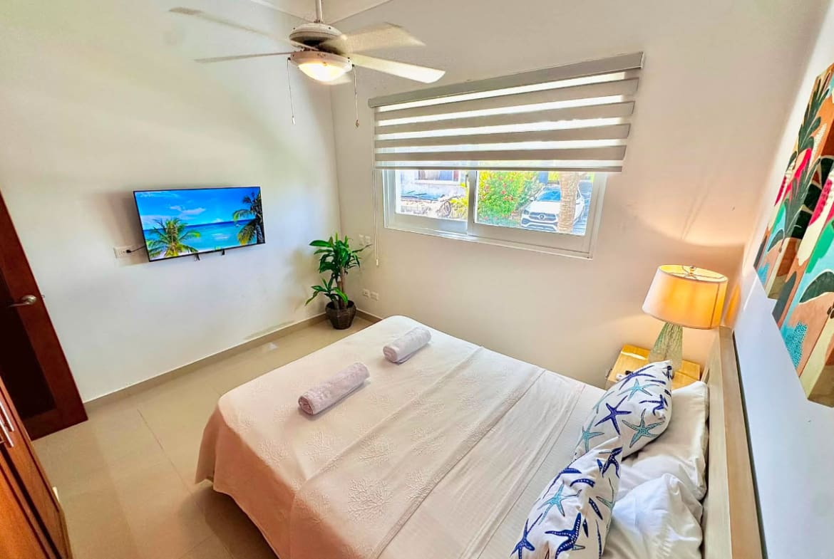 Cozy bedroom with a queen bed, TV, and tropical art