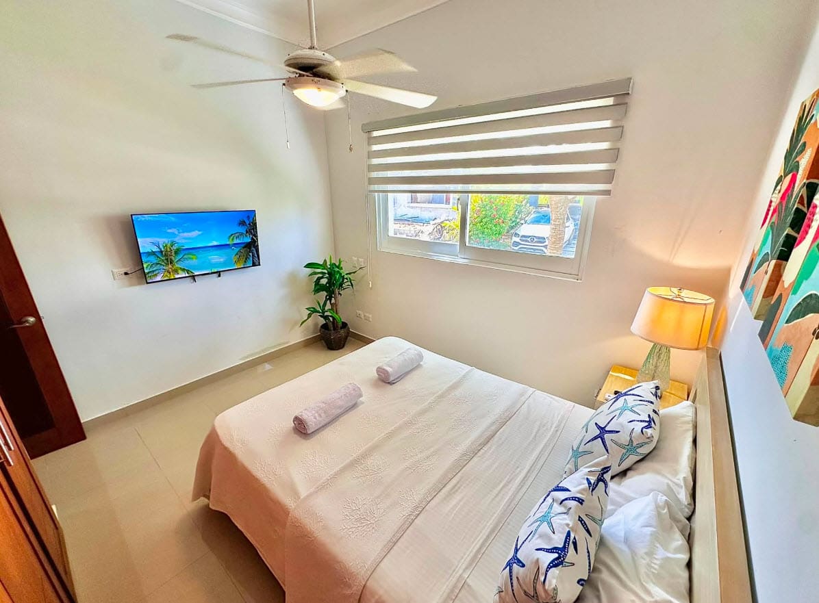 Cozy bedroom with a queen bed, TV, and tropical art