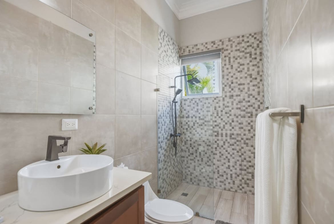 Modern bathroom with white sink, toilet, and tiled shower.