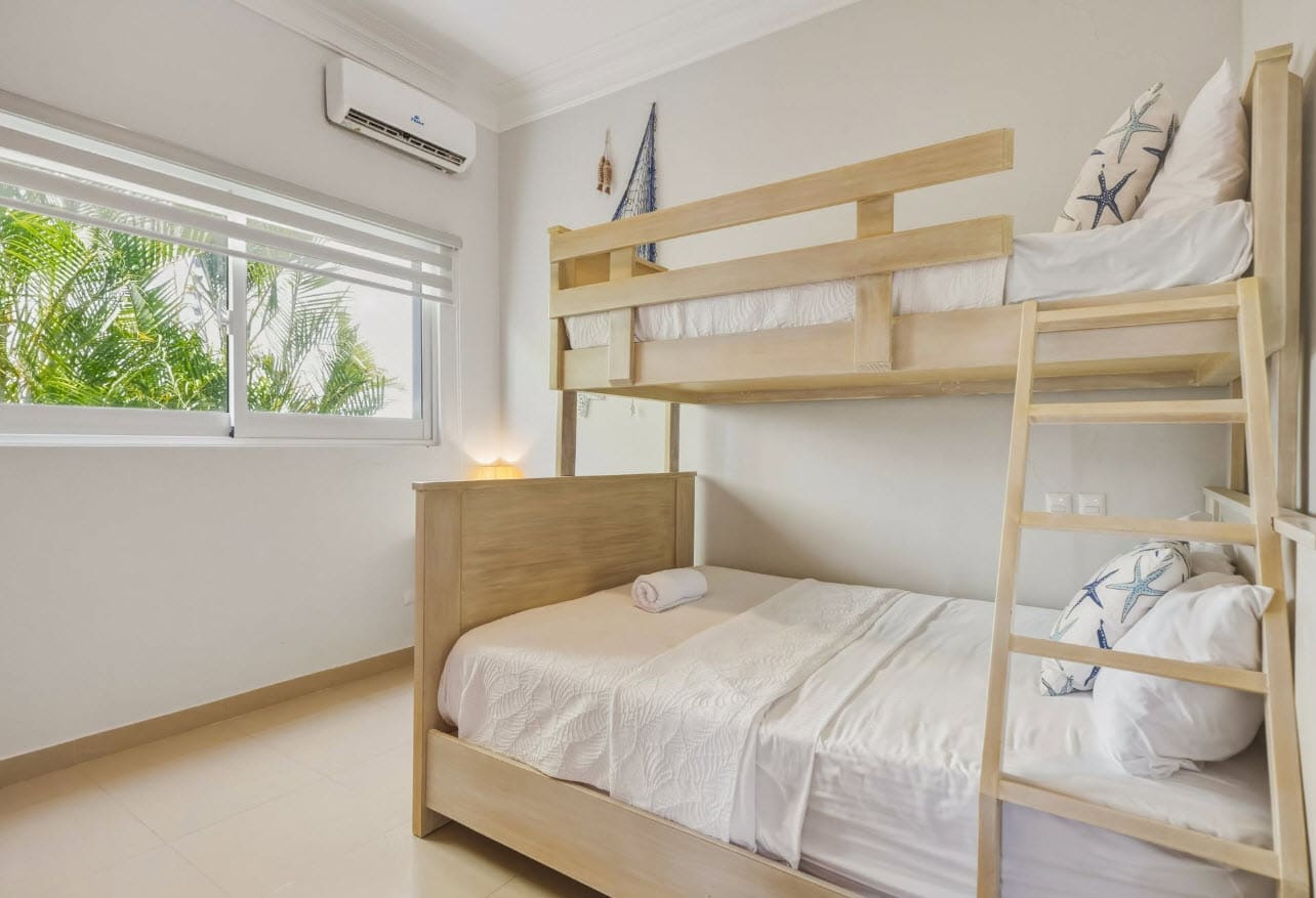 Light wood bunk beds with white bedding in a bright bedroom with a large window.