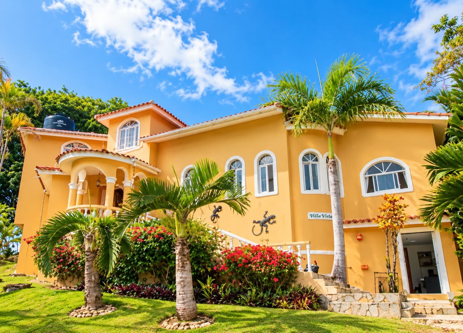 Yellow villa with palm trees and tropical flowers, "Villa Vista" sign