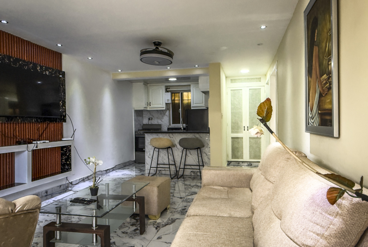Modern living room with sofa, glass coffee table, and open-plan kitchen