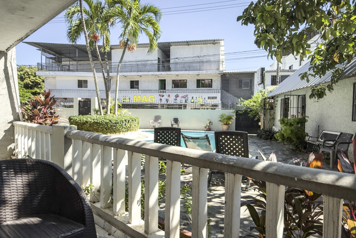Courtyard with pool, chairs, and tropical plants outside a building.