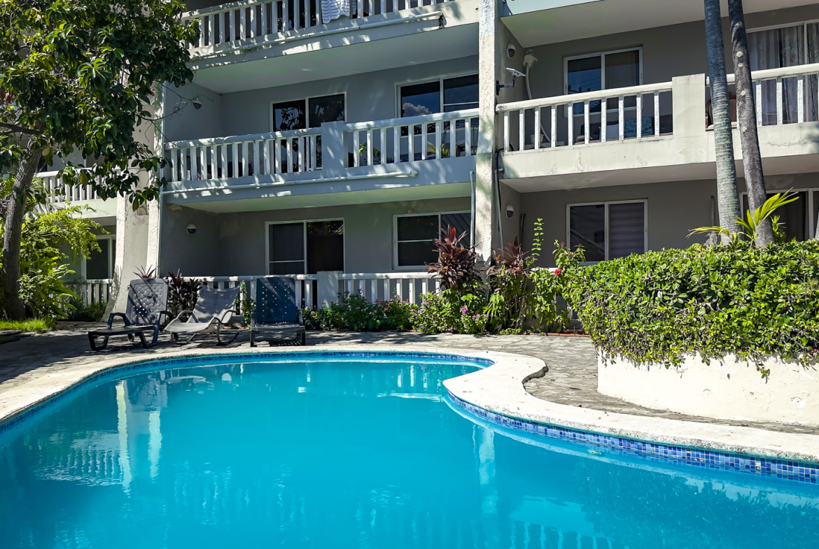 Resort swimming pool with lounge chairs and a modern building in the background.