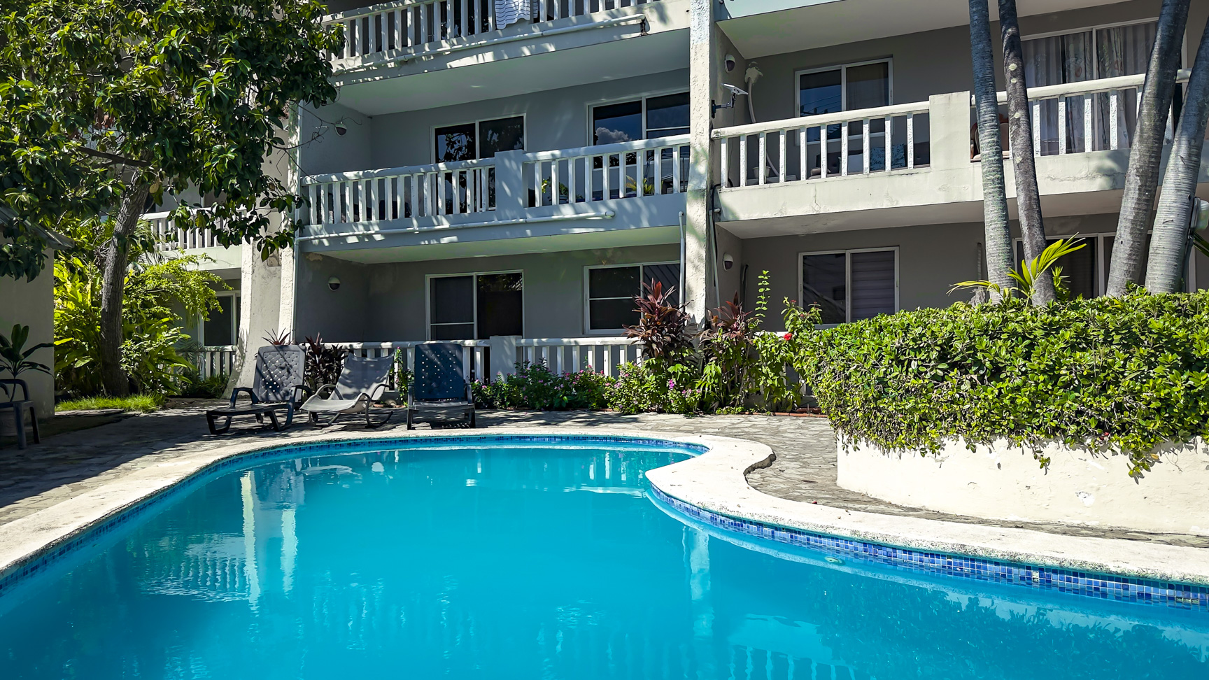 Resort swimming pool with lounge chairs and a modern building in the background.