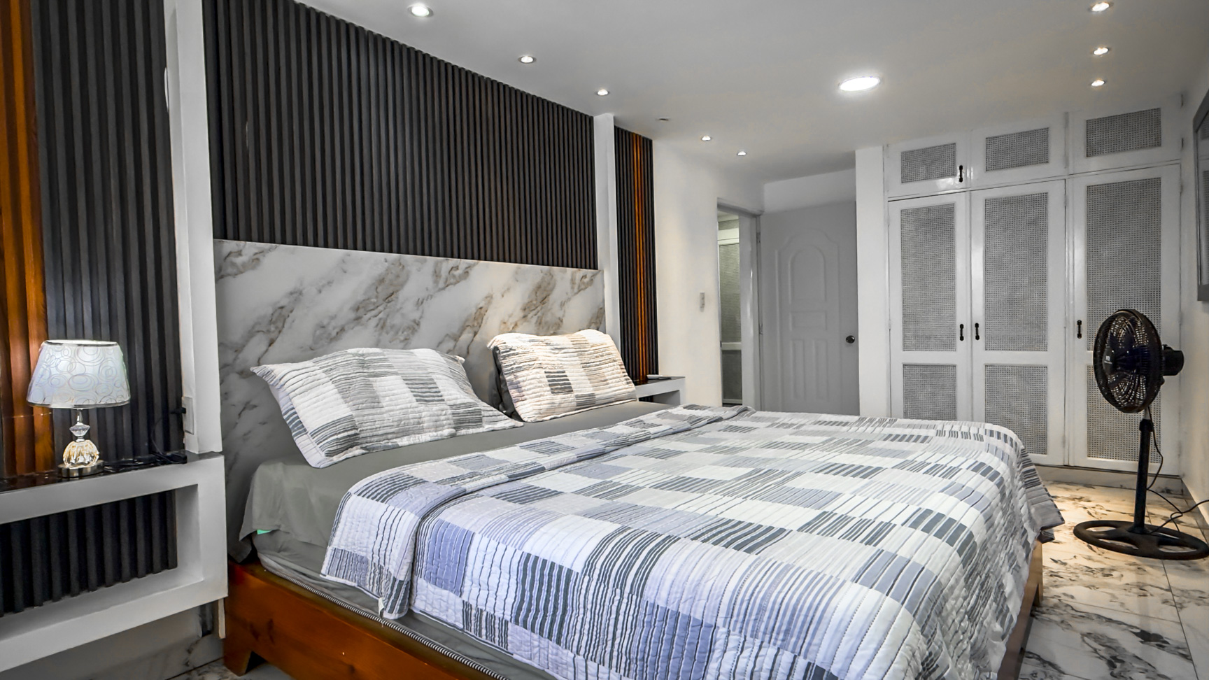 Modern bedroom with a marble headboard, striped bedding, and white wardrobes.