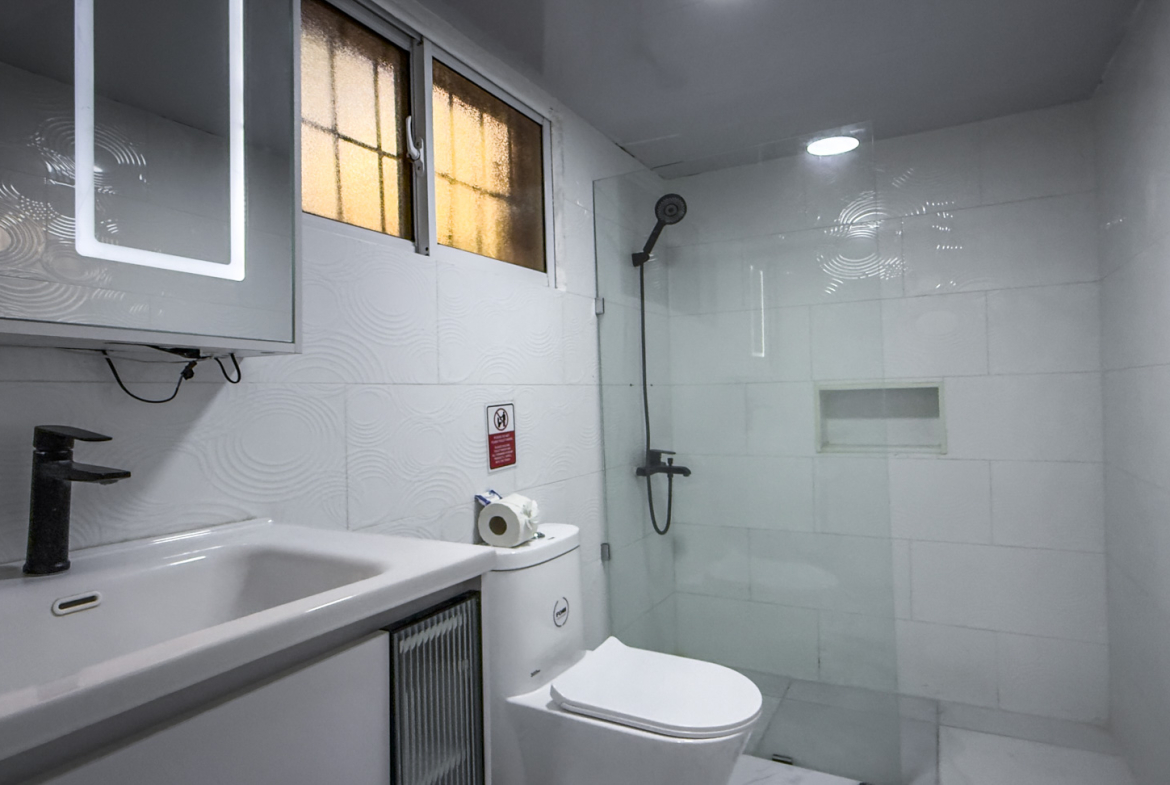Modern white bathroom with a sink, toilet, and glass-enclosed shower.