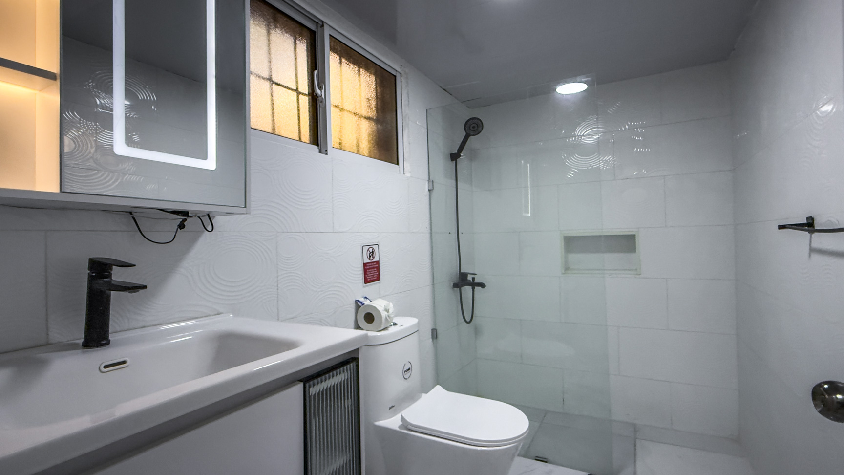 Modern white bathroom with a sink, toilet, and glass-enclosed shower.